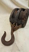 Close-up photo showing the wooden block and metal hook of the antique pulley with visible wear and rust.