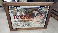 Full frontal view of the large Coca-Cola advertising mirror with wood frame and printed text/image on mirror surface.