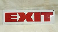 Front side of the rectangular tin exit sign showing red capital letters on white background with mounting holes at corners.