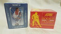 Two factory sealed hockey card sets side by side, one in a blue box labeled Future Sensations Factory Set with a hockey player image, the other in an orange box labeled 1990 NHL Score Rookie and Traded 180 Player Card Set featuring a hockey player silhouette.