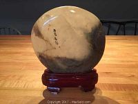 Front view of the polished decorative stone with East Asian script and wooden stand on a wooden table.