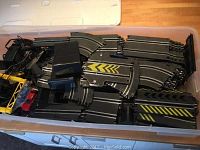 Overall view of modular black plastic race track pieces and accessories inside clear box with white lid.
