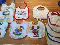Photo showing seven baby bibs with various prints and trims laid flat on wooden surface.