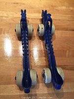 Top-down view of two blue plastic roller skate guards with white wheels, showing overall length and shape.