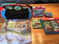 Photo of the full lot displaying the large Thomas plush pillow, duvet cover, lunch pail, soft football, DVDs, plastic pen case, and Aqua Doodle mat with drawing tools.