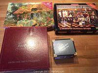 Wide shot of all four items: Trivial Pursuit Baby Boomer Edition box, Reel to Reel Trivia Game box, and two 1000-piece puzzle boxes depicting a cottage and general store interior.