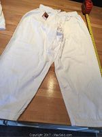 White karate pants laid flat on a wooden surface showing full length and elastic waistband partially in frame with measuring tape.