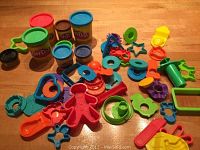 Play-Doh containers and various plastic molds and cutters laid out on wood surface.