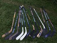 Photo of 11 boys' hockey sticks laid on grass showing variety of sizes and blade colors