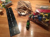 Wooden train tracks, toy train, and road pieces laid out on a wood surface, with some items in plastic bags.