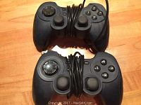 Top view of two black PC controllers showing analog sticks, directional pads, and numbered buttons.