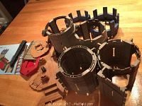 Multiple gray plastic castle towers and wall sections, brown drawbridge parts, ladders and smaller accessories arranged on wood table