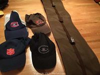 Four caps including brown, blue, two black caps and a brown fabric hanging cap holder with buckles.
