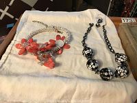 Photo showing two necklaces laid on fabric: a pink flower statement necklace with beads and a black and white polka dot bead necklace with matching earrings on a card.