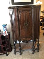 Front view of vintage wooden cabinet showing closed double doors and ornate carved details on doors, legs, and lower edge.
