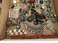 Top-down photo showing a mix of vintage costume jewelry including earrings, necklaces, brooches, and beads placed in a box.