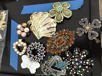 Top view of 10 vintage brooches laid out on black surface showing variety of colors and shapes.
