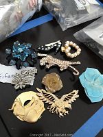 Photo showing 9 vintage Trifari brooches including floral, animal and pearl designs arranged on a black surface.