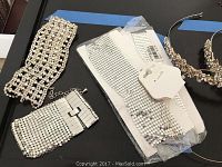 Photo of silver mesh bracelets, silver tone headband with white stone, and rhinestone headbands on black surface