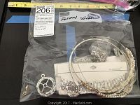 Photo shows formal wear accessories including silver mesh bracelets sealed in plastic, silver-tone hoops, and a large clear faceted pendant.