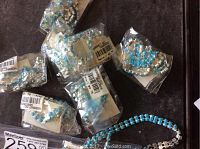 Photo showing multiple blue stone necklaces and earrings sealed in individual plastic bags on a surface.