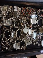 Overview of assorted new silver-tone beaded and charm bracelets with original tags laid out on dark surface.