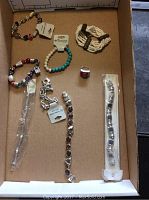 Overview photo of assorted bracelets in box showing various styles including metal chain bracelets, beaded bracelets and woven bracelet, all with tags shown.