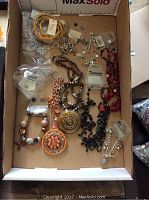 Photo of box containing multiple bracelets and necklaces in different designs and materials, some with tags still attached.