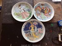 Three Limoges porcelain plates shown flat on a dark surface, each decorated with a hand-painted fashion illustration of different women in period costumes.