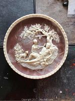 Decorative, marbled brown and cream collector's plate showing a classical scene of two figures under a tree with a goat in raised relief.