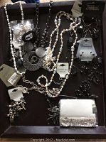 Top view of assorted necklaces, earrings, and bracelets arranged on dark surface showing various styles and tags attached confirming items are new.