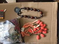 Top-down view of multiple necklaces, a bag of assorted beads or jewelry components on cardboard surface
