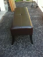Full angled profile showing leatherette bench top and curved legs, scratches faintly visible on top surface.