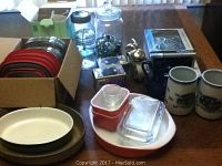 Overview of the lot showing various glassware, ceramic mugs, baking, and kitchen items along with boxed clocks and electronic scale.