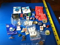Multiple Olympic and Canadian themed pins displayed on a table with measuring tape showing size.