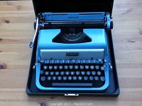 Blue Underwood Golden Touch typewriter inside black case placed on wooden table.