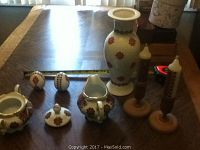Photo shows full view of set on a table: two candles on wooden holders, salt and pepper shakers, sugar bowl with lid, creamer, and flower vase with a red and brown traditional Ukrainian style pattern.