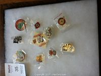 Photo showing nine distinct Little League pins arranged on white background, some still in plastic wrapping.