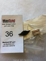 Photo showing both airline pins with a MaxSold auction tag number 36. Pins include a black Bradley First Air wing pin and a rectangular Air Transat pin.