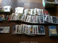 Large assortment of football and basketball cards spread on a floor, grouped in multiple stacks and loose piles.