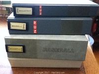 Four large binders stacked, showing labels indicating card sets inside and the word BASEBALL embossed on one binder.
