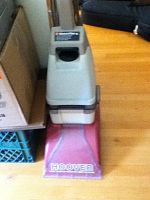 Front view showing Hoover logo on red base of carpet cleaner with upper grey housing and handle.