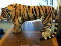 Side profile of the large tiger figurine standing on a wooden surface by a window, showing full length and detailed stripes.