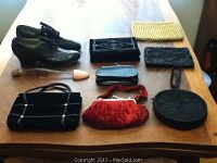 Seven purses and one pair of black leather shoes displayed on wooden table. Includes yellow woven purse, velvet and beaded black purses, red velvet purse, and vintage shoes with one shoe form.