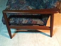 Side view of loveseat showing teak armrest, base and floral cushion.