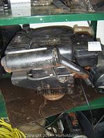 Side view of 11 HP Briggs and Stratton gas engine showing air intake mesh, pull start, electric starter cable, and pulley on bottom. Engine is black with wear.