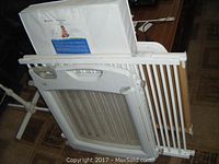 Wood crib frame stacked with white mattress and plastic baby/pet gate showing slats and locking handle.