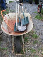 Older metal wheelbarrow filled with tools on gravel surface, showing overall lot contents
