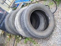 Four used tires stacked on gravel, showing tread wear and brand visible on each tire sidewall.