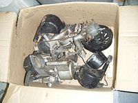 Box containing assorted used gas engine recoil starters and one used carburetor with visible wear and aging.